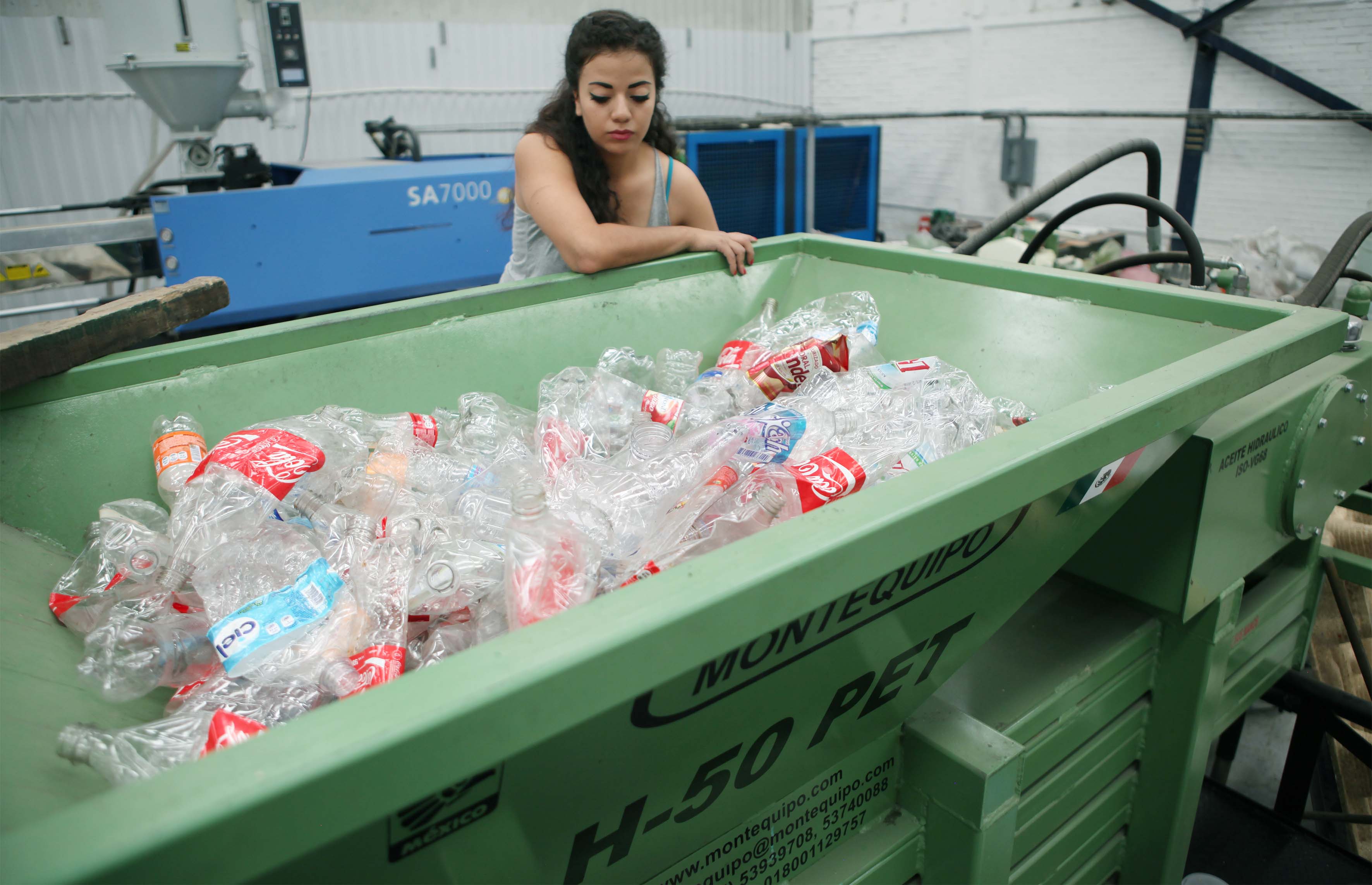Mujer junto a contenedor lleno de botellas de plastico 