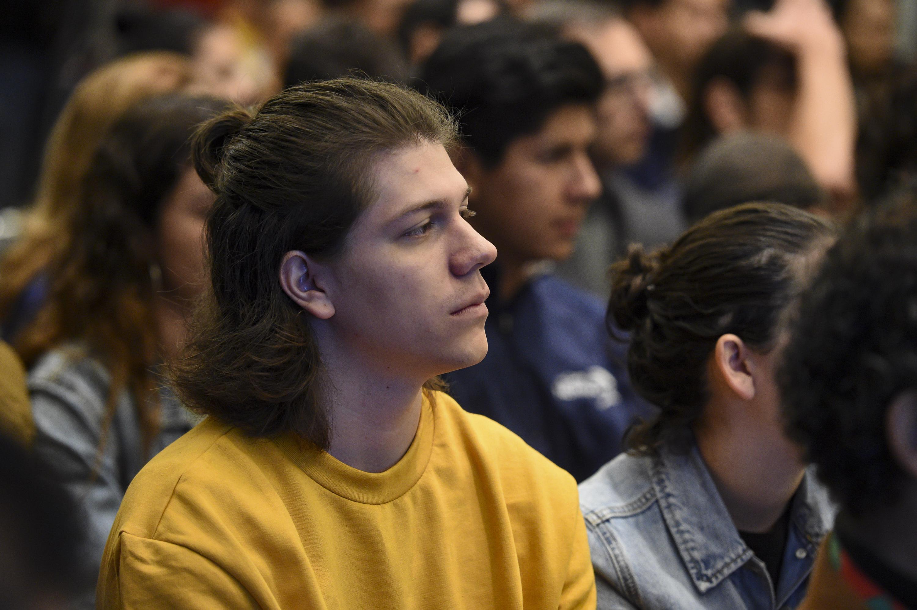 Un joven con sueter amarillo entre el publico asistente al anuncio